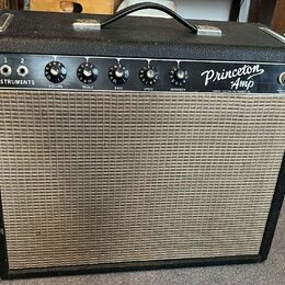 Kytarový zesilovač v černém krytu s béžovou textilní mřížkou. Na ovládacím panelu je nápis Princeton Amp a Fender Electric Instrument Co., dále označ…