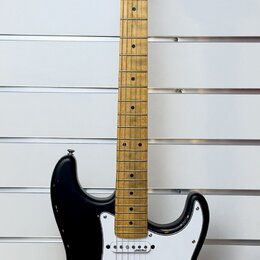 Černá elektrická kytara s bílým pickguardem a hnědým javorovým hnedkem. Na hlavě je nápis "Squier" a "Affinity Series". Tělo kytary vykazuje známky o…