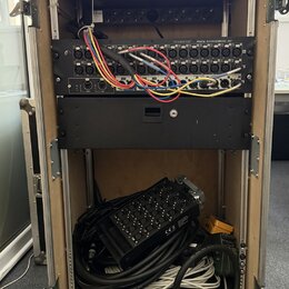 Otevřený transportní rack na kolečkách, v němž jsou namontovány dvě černé zařízení. Horní jednotka nese nápis Soundcraft MINI STAGEBOX 32 a má zapoje…