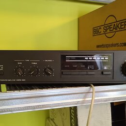 Černý stereofonní zesilovač s nápisem TESLA STEREO INTEGRATED AMPLIFIER AZS 223. Na předním panelu jsou ovládací prvky pro basy, treble a balance, př…