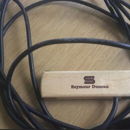 Na fotografii je vidět černý kabel a k němu připevněný obdélníkový dřevěný blok světlé barvy. Na bloku je vyryto logo a nápis Seymour Duncan. Povrch…
