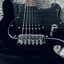 Černá elektrická kytara s tvarem typu Stratocaster a hnědým hmatníkem. Nástroj má jeden viditelný snímač typu humbucker v pozici u mostu a chromovaný…
