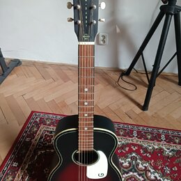 Akustická kytara s černým povrchem a červeným přechodem v oblasti středu. Na hlavě je bílý nápis GREISCH® a pod ním svisle napsaný model JIM + DANDY,…