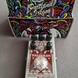 Šedý kytarový efekt v kovovém šasi s červeným grafickým panelem. Na panelu je nápis TALISMAN a v dolní části logo catalinbread s doplňkem MECHANISMS…