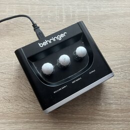 Černý kompaktní přístroj značky behringer s třemi bílými otočnými knoflíky. Na spodní straně jsou viditelné nápisy MIC/LINE GAIN 1, INST GAIN 2 a OUT…