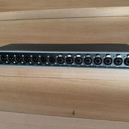 Šedý rackový audio přístroj s černým horním krytem. Na zadním panelu jsou umístěny konektory XLR a dva konektory Ethernet s nápisy SEND a RETURN. V l…
