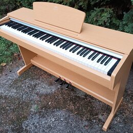 Digitální piano v dřevěné barvě s klasickým provedením. Nástroj má bílé a černé klávesy, tři sustain pedály a nápis "KORG" na horním víku. Povrch nás…
