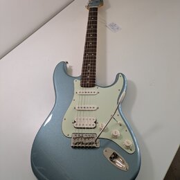 Modrá elektro kytara s kovovými stupeničky a bílým pickguardem. Na hlavě je viditelné logo Fender. Nástroj má tři snímače, tři ovládací knoflíky a tř…