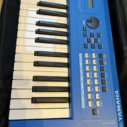 Modrý syntezátor s klaviaturaí, umístěný v černém pouzdře. Na pravé straně je svisle napsáno YAMAHA a v dolní části nápis MUSIC SYNTHESIZER mx49 spol…