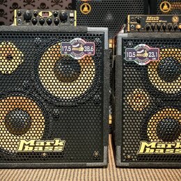 Dvě basové reproduktorové skříně značky Mark bass v černé barvě s kovovými mřížkami. Levá skříň má dva reproduktory a nálepy s nápisy 17,5 kg / 38,6…