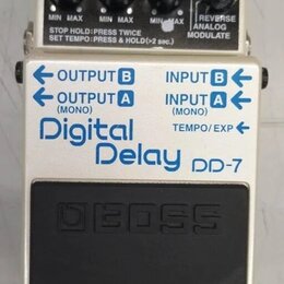 Kytarový efekt pedál značky BOSS, model Digital Delay DP-7. Zařízení má bílé tělo s modrými nápisy a čtyři tyrkysové ovrtovací knoflíky. Na horním če…