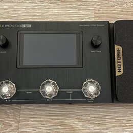 Černý efektový procesor s nápisem AMPERO ONE a doplňkem Amp Modeler / Effects Processor. Zařízení má centrální displej, dva otočné knoflíky s popisky…