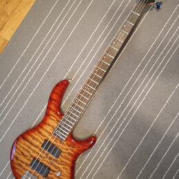 Elektrická basová kytara s tělem z masivního dřeva s výraznou plamenovitou strukturou v červenohnaté barvě. Na hlavě je viditelné logo Ibanez a nápis…