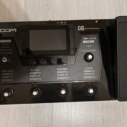 Černý kytarový procesor s karbonovým povrchem a připojeným pedálem značky ZOOM. Na přístroji je nápis G6 Multi-Effects Processor a několik ovládacích…