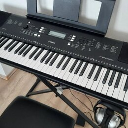 Černý digitální klavír s bílými a černými klávesami, umístěný na černém X-stojanu. Na ovládacím panelu je bílé logo YAMAHA a nápis EW300. V horní čás…