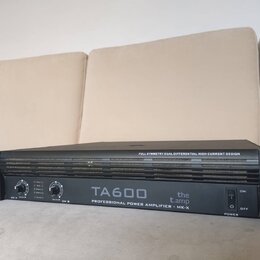 Černý rackový výkonový zesilovač s úchyty po stranách. Na předním panelu je bílý nápis TA600, logo the t.amp a text PROFESSIONAL POWER AMPLIFIER - MK…