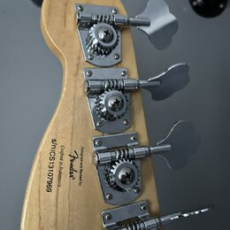 Zadní strana hlavy basové kytary z přírodního dřeva se čtyřmi chromovanými ladičkami. Na dřevě je černý nápis: Designed and Backed by Fender, Crafted…