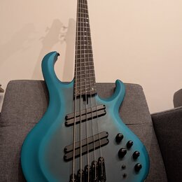 Modrá basová kytara s pětistrunným hmatníkem a dvěma humbuckery. Tělo má matný povrch s tmavším stínováním v oblasti středové části. Na těle jsou umí…