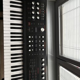 Černý synthesizér s klaviaturaí, na jehož horním panelu je bílý nápis HYDRASYNTH a logo MOOG. Přístroj obsahuje množství ovládacích knoflíků, posuvní…