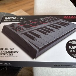 Fotografie zachicuje krabici s produktem AKAI MPKmini SPECIAL EDITION GREY. Na obalu je zobrazen šedý kompaktní MIDI kontrolér s klávesami, osmi červ…