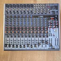 Stříbrný mixážní pult značky behringer s označením XENYX 2442USB. Zařízení obsahuje numerous vstupní konektory, posuvníky a ovládací knoflíky v modré…