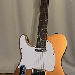 Kytara typu Telecaster v matné bronzové barvě s bílým pickguardem. Na krytu snímače je viditelný nápis "Fender". Nástroj je umístěn na černém stojanu.