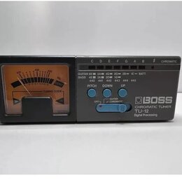 Digitální chromatický ladič v černé barvě s analogovou stupnicí. Na pravé straně je nápis BOSS CHROMATIC TUNER TU-12 Digital Processing. Horní panel…