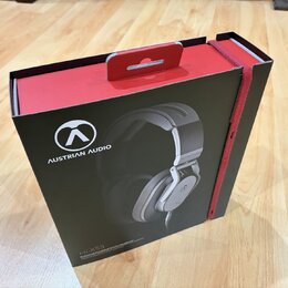 Černá cardboardová krabice s červenými prvky a úchytkou v horní části. Na přední straně je bílé logo a nápis AUSTRIAN AUDIO, fotografie sluchátek a v…