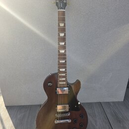 Hnědá elektrická kytara s tvarem singlecut a tmavým hracím hředcem. Na hlavě je bílé logo Gibson a nápis Made in USA. Kytara má dva humbuckery, čtyři…