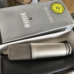Stříbrný kondenzátorový mikrofon s kovovou síťkou, na jehož těle je nápis Made in Australia. Mikrofon leží v bílém boxu na černém koženěném pouzdře.…