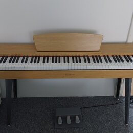 Digitální piano v dřevěném provedení s bílými a černými klávesami. Na středové liště pod klaviaturou je nápis HENRY'S. Nástroj stojí na čtyřech šedýc…