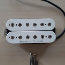 Bílý humbucker s dvěma řadami šesti polových magnetů. Na spodním rámečku je černý nápis Seymour Duncan. K snímači vede černý kabel a vedle něj jsou p…