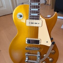 Zlatá elektrická kytara s jednodrážkovým tělem a bílým plechtrzem. Nástroj je vybaven dvěma humbuckery, chromovaným mostem s tremolo páčkou a čtyřmi…