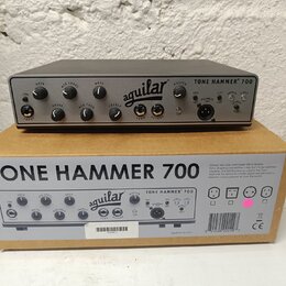 Šedý basový předzesilovač s nápisem TONE HAMMER 700 a logem aguilar. Zařízení má několik ovládacích knoflíků s popisky GAIN, MID LEVEL, BASS, DRIVE,…