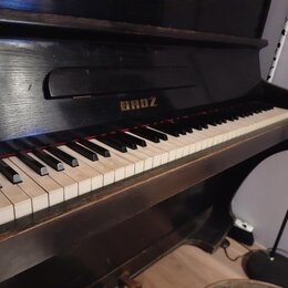Černý pianino s klaviatura z bílých a černých kláves. Nad klávesami je v horní části nápis BROZ. Povrch nástroje vykazuje drobné škrábance a opotřebe…