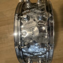 Stříbrný kovový snare drum s chromovaným povrchem. Uprostřed korpusu je kulatý štítek s nápisy MAPEX a MPX STEEL. Povrch nástroje vykazuje výrazné zn…