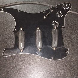 Černý plastový pickguard pro kytaru s třemi černými snímači. Na každém ze snímačů je bílý nápis "Wilkinson". Součástí jsou tři černé ovládací knofíky…
