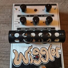 Kytarový efekt s bílým kovovým šasi a černými ovládacími knoflíky. Na spodní části je velký nápis Wiggler a logo electro-harmonix s textem MADE IN NY…