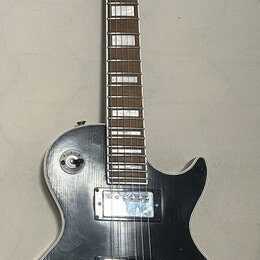 Černá elektrická kytara typu Les Paul s bílým lemováním korpusu. Na hlavě je viditelné logo Ligmand. Nástroj má dva humbuckery, čtyři ovládací knoflí…