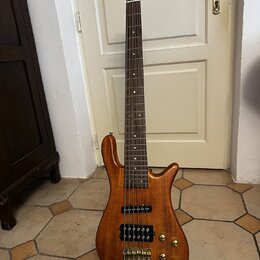 Šeststrunná basová kytara s přírodním dřevěným povrchem a hnědým hmatníkem. Na těle jsou umístěny dva humbuckery, čtyři zlaté potenciometry a zlatý m…