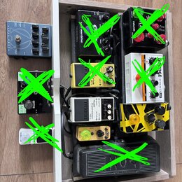 Fotografie zobrazuje několik kytarových efektů v dřevěné šasi a vedle něj. V šasi jsou umístěny pedály s nápisy "overdrive", "NUX", "DRIVE" a "Noise…