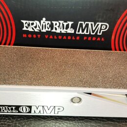 Kytarový pedál s hliníkovým šasi a hrubou, protiskluzovou povrchovou úpravou na horní části. Na boku je uveden nápis ERNIE BALL MVP. V pozadí je vidě…