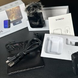 Sada bezdrátového mikrofonu značky SYNCO v originálním bílém balení. Obsahuje černý vysílač s nápisem SYNCO Transmitter a chlupatým windscreenem, čer…