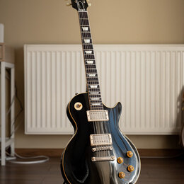 Černá elektrická kytara s jednovýstupním tělem a hnědým lemováním. Na hlavě je zlatý nápis Gibson. Kytara má dva humbuckery, čtyři otočné knoflíky a…