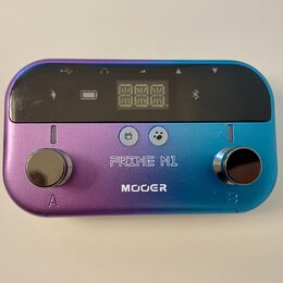 Multiefektový pedál v kovovém provedení s barevným přechodem od fialové k modré. Na horní straně je černý displej s ikonami baterie a Bluetooth, pod…