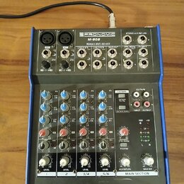 Mixážní pult s modrým šasi a stříbrným předním panelem. Na horní části je nápis PRONOMIC M-602 PREMIUM 6-INPUT 2-BUS MIXER. Zařízení obsahuje různé v…
