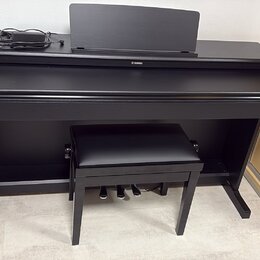 Černý digitální piano v černém nábytkovém stojanu s přívodním kabelem a doprovodnou černou stolečkou. Na přední straně je umístěno logo YAMAHA. Nástr…