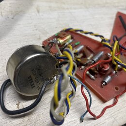 Fotografie zobrazuje elektronickou součástku v kovovém pouzdře připojenou k červené desce s dalšími komponenty a barevným zapojováním kabelů. Na kovo…
