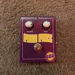 Fialový kytarový efekt s dvěma bílými otočnými knoflíky. Na šasi jsou nápisy VOLUME a FUZZ s číslováním 0–10, velký žlutý nápis FREE FUZZ TM a v prav…