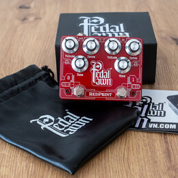 Červený kytarový efekt s nápisem Pedal lawn a REDPRINT. Na horní straně jsou čtyři kovové otočné knoflíky s popisky Volume, Drive, Volume a Drive, dá…
